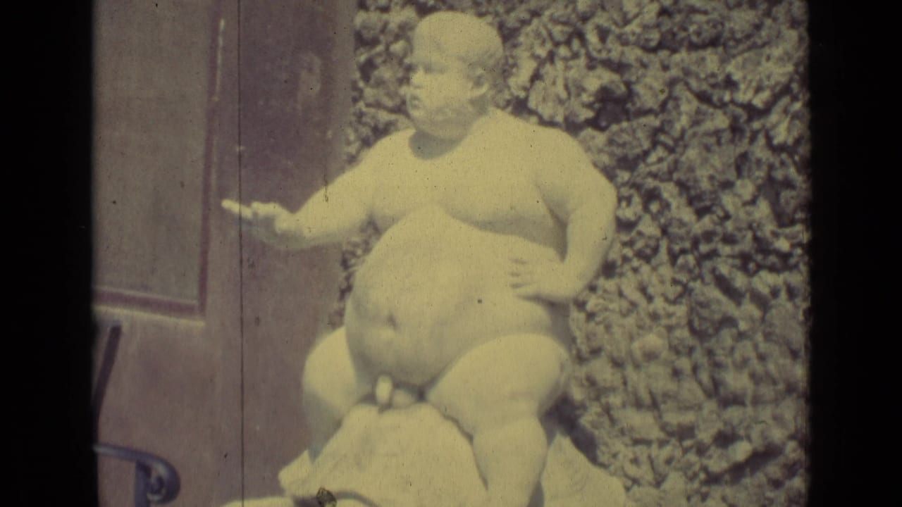 1962 Florence 8mm frame showing a plump nude boy statue riding a turtle near a textured stone wall and metal railing.