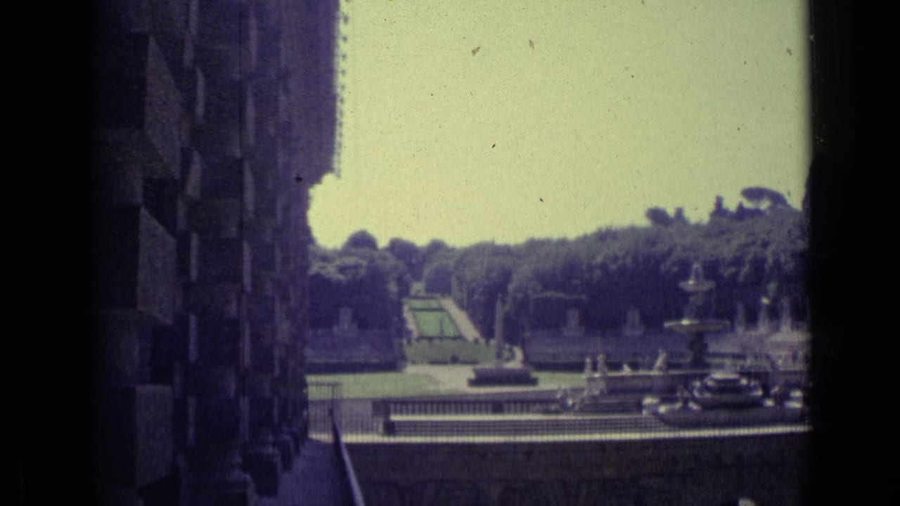 Formal garden and fountain seen from a shaded stone building edge.