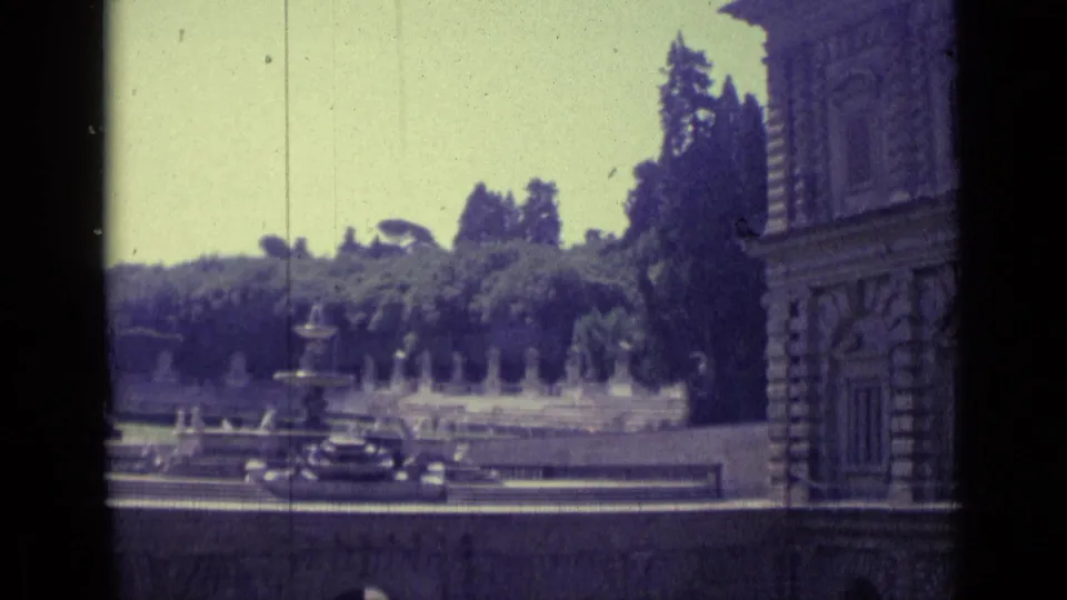 1962 Florence frame showing an ornate stone facade at right, fountains, garden terraces, trees, and dark cars in the foreground.