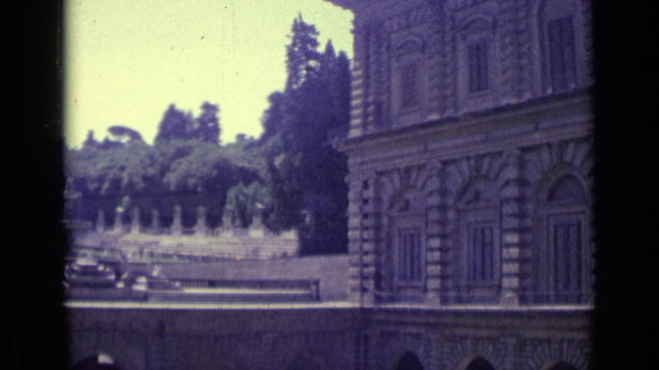 Stone palace facade beside a garden fountain and tree-lined terrace.