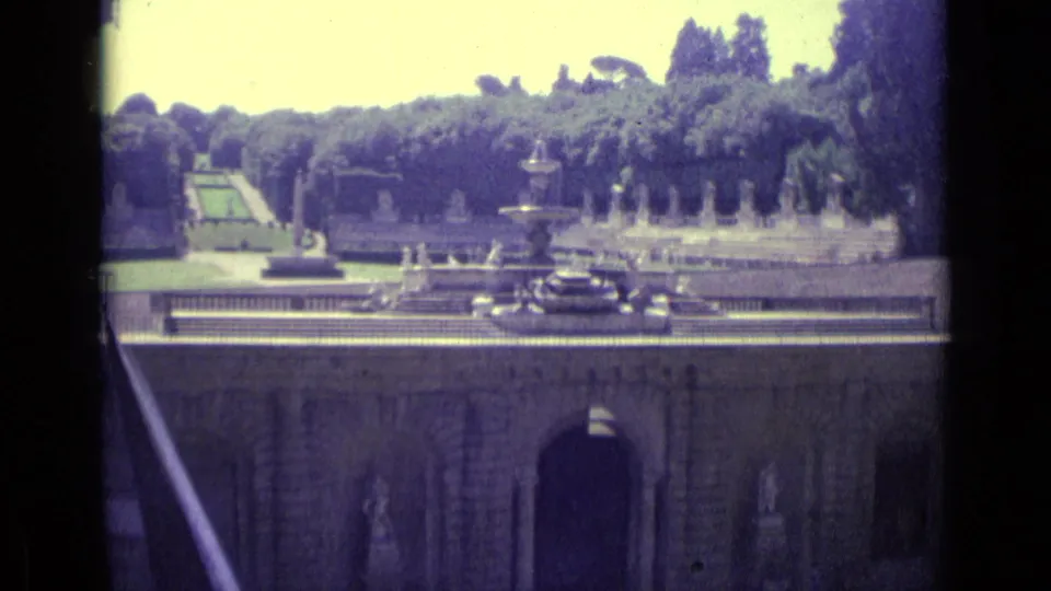 1962 Florence garden frame with a multi-tiered fountain, stone terrace, statues, greenery, and palace lower wall.
