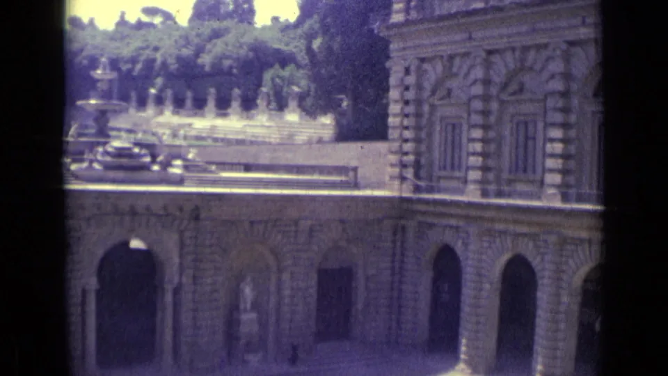1962 Florence frame of a grand stone facade with arches and shuttered windows, with a fountain and garden visible behind.