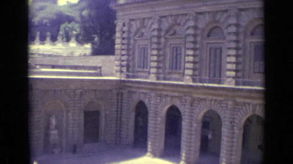 1962 8mm Florence frame showing the building facade more closely, with arched openings, shuttered windows, and courtyard paving.