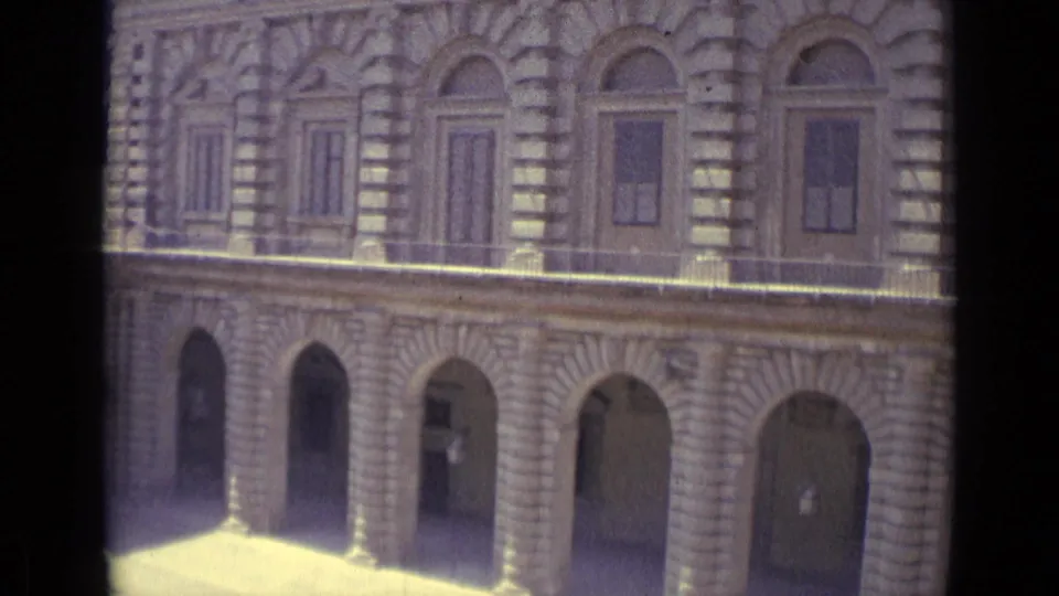 1962 Florence home-movie view of an ornate stone facade with arched openings and shuttered upper windows, partly blocked by dark window framing.