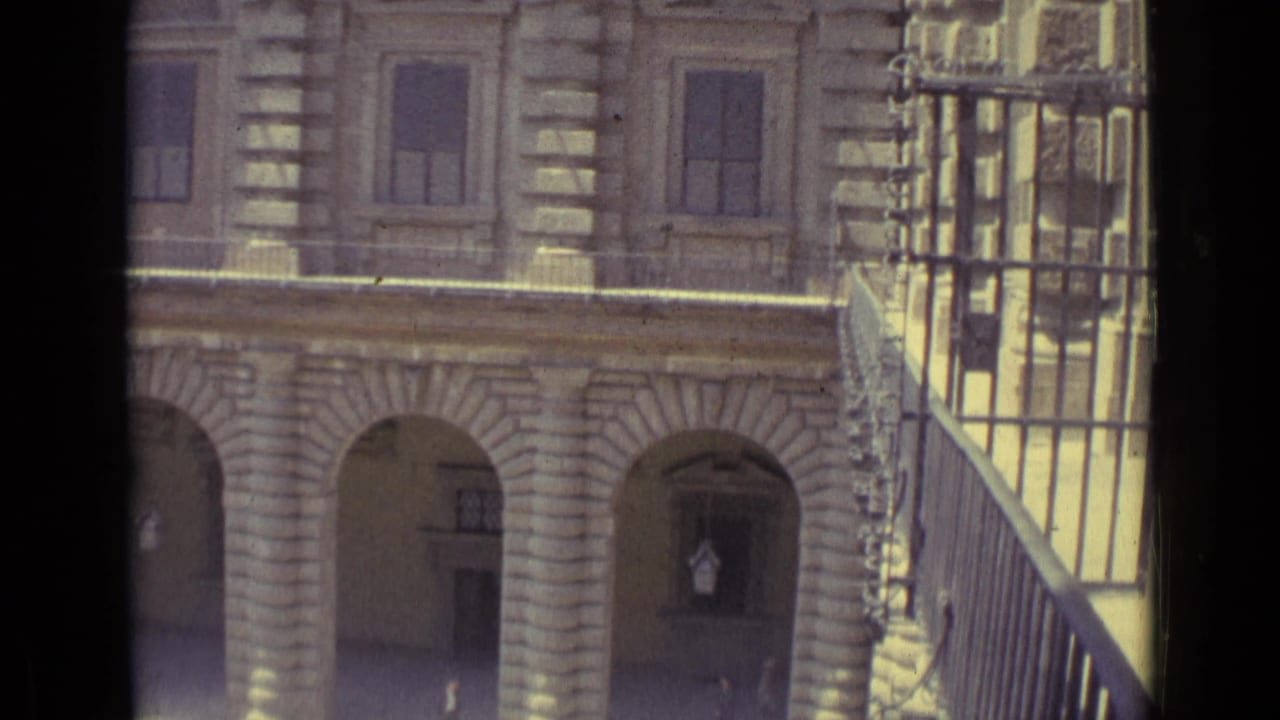 1962 Florence home-movie frame showing a sunlit historic facade with arched openings, tall windows, and a dark iron railing.