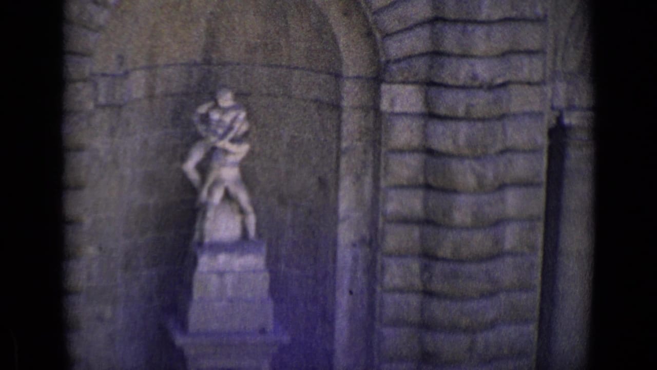 Stone statue of two figures on a pedestal inside an arched niche.