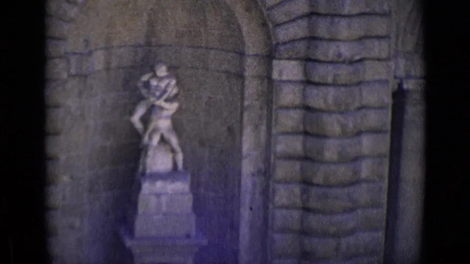 1962 Florence 8mm frame showing a weathered stone sculpture of two figures on a pedestal within an arched masonry niche.