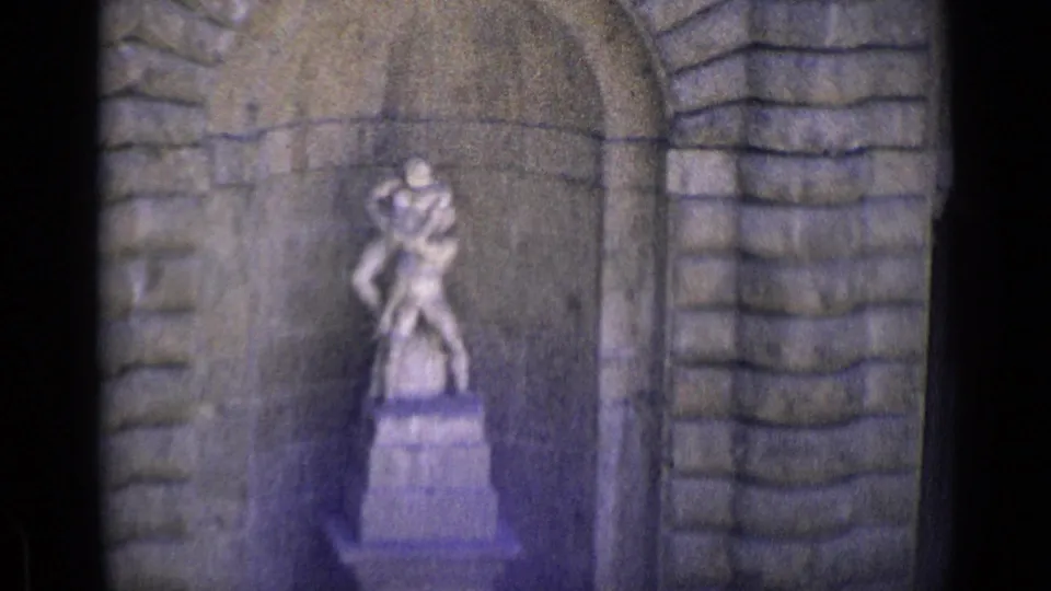 1962 Florence home-movie frame with a two-figure stone statue centered in a recessed arch and flanked by rough stone blocks.