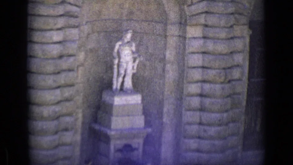 1962 Florence 8mm frame showing a standing male stone statue on a pedestal, set against an arched niche and flanked by block masonry.