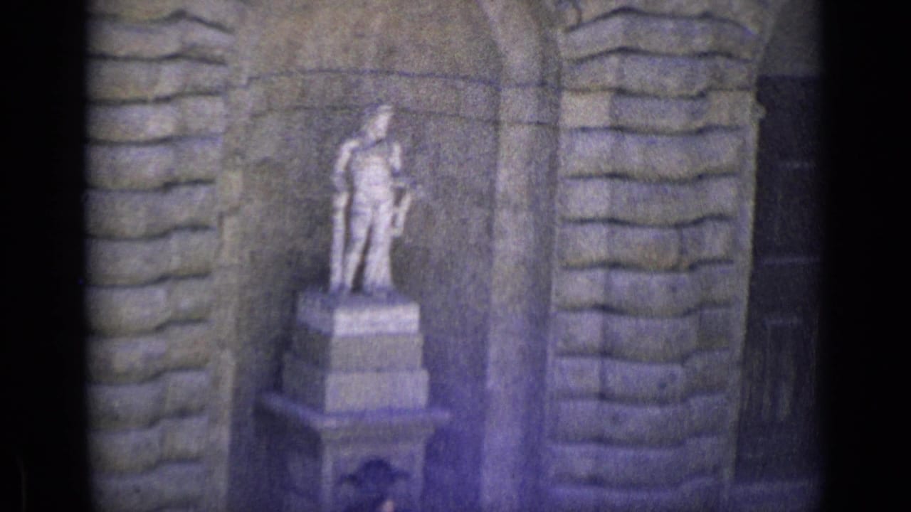 Stone statue standing in a niche beside rough masonry walls.