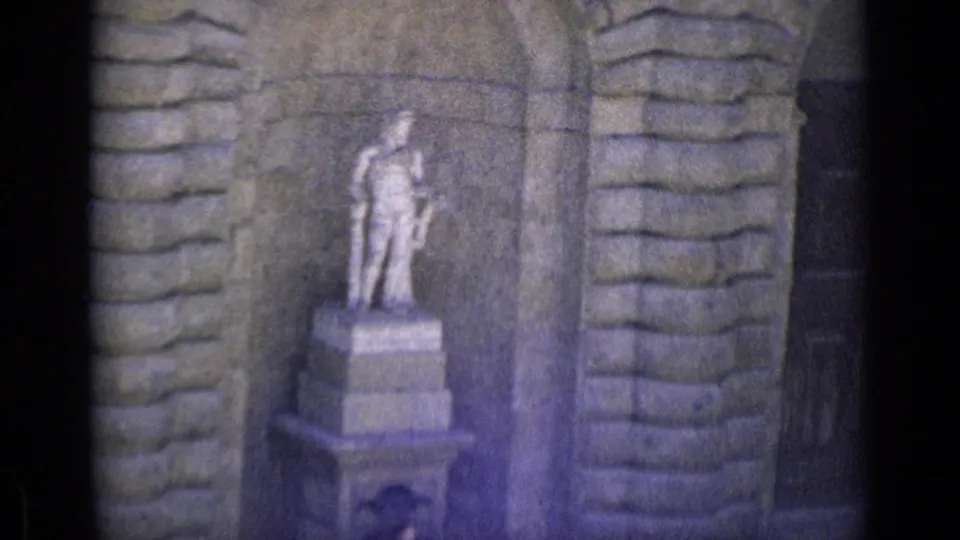 1962 Florence home-movie frame showing a classical stone statue in a wall niche, filmed with soft 8mm focus and dark edge vignetting.