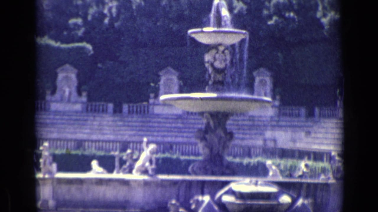 Tiered garden fountain with water spraying and statues around the basin.