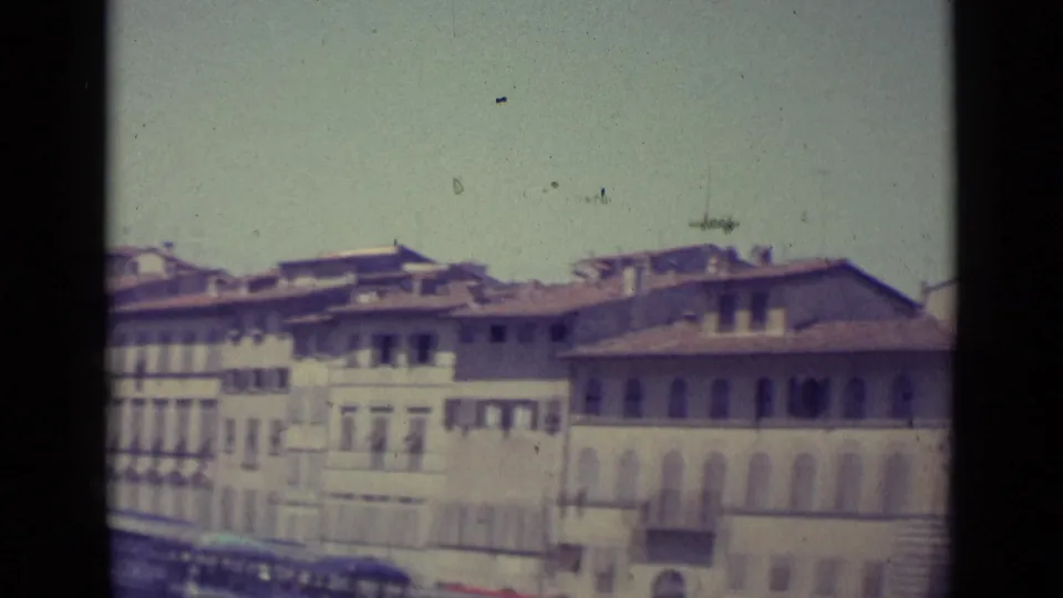1962 Florence home-movie frame showing upper facades, rooflines, shuttered windows, and dark 8mm film borders.