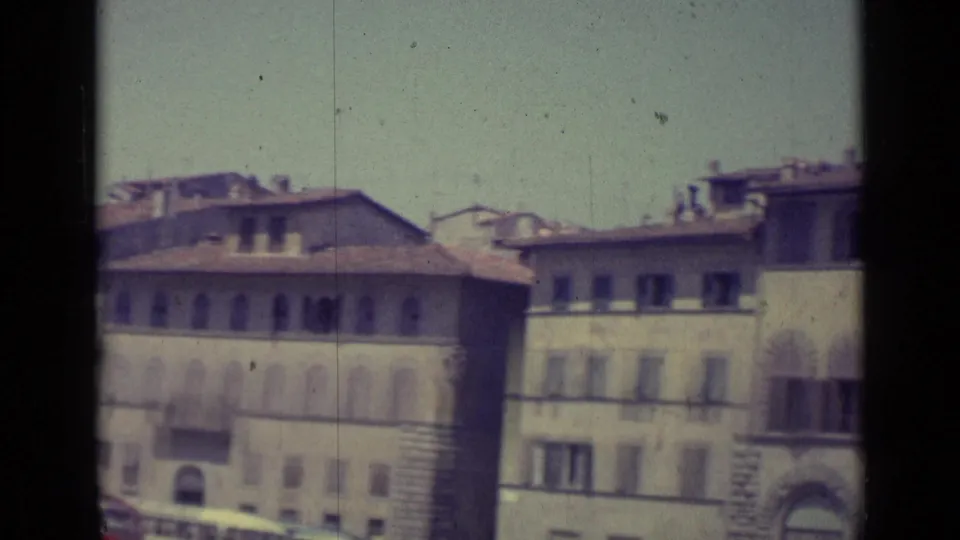 1962 Florence frame with pale masonry buildings, arched upper windows, shutters, tiled roofs, and visible film grain.