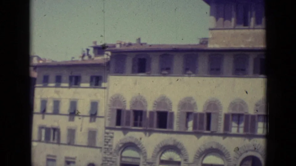 1962 Florence home-movie frame showing shuttered windows, decorative arched stonework, and adjacent masonry buildings.