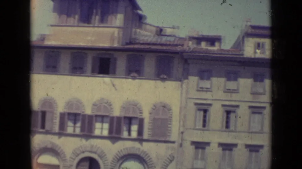 1962 Florence home-movie frame showing historic building facades with shutters, arched openings, pale walls, and terracotta rooflines.