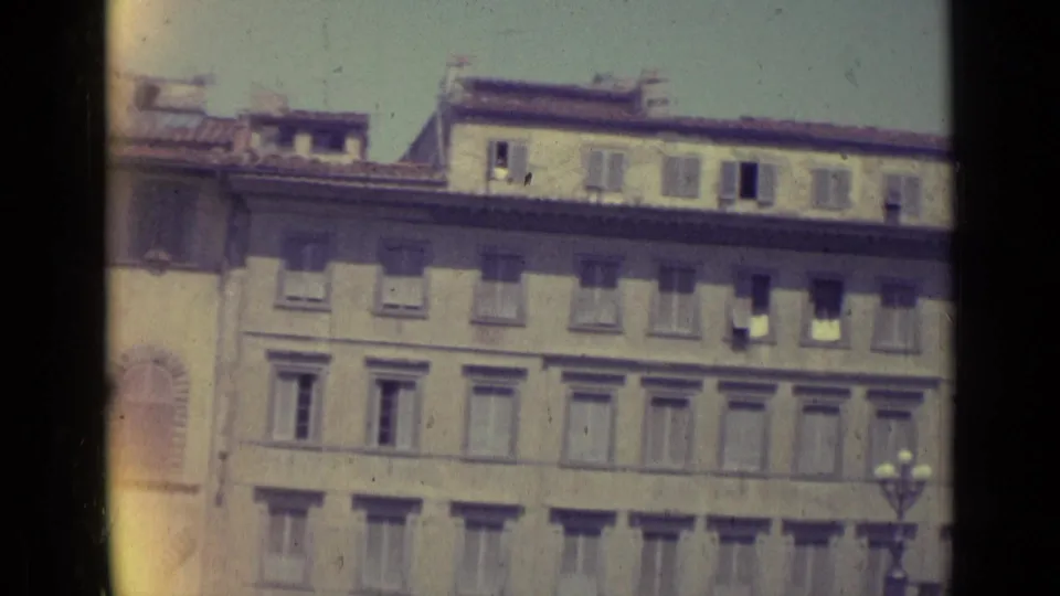 1962 Florence view of a long historic facade with shuttered windows, upper roof structures, and a streetlamp at the edge.
