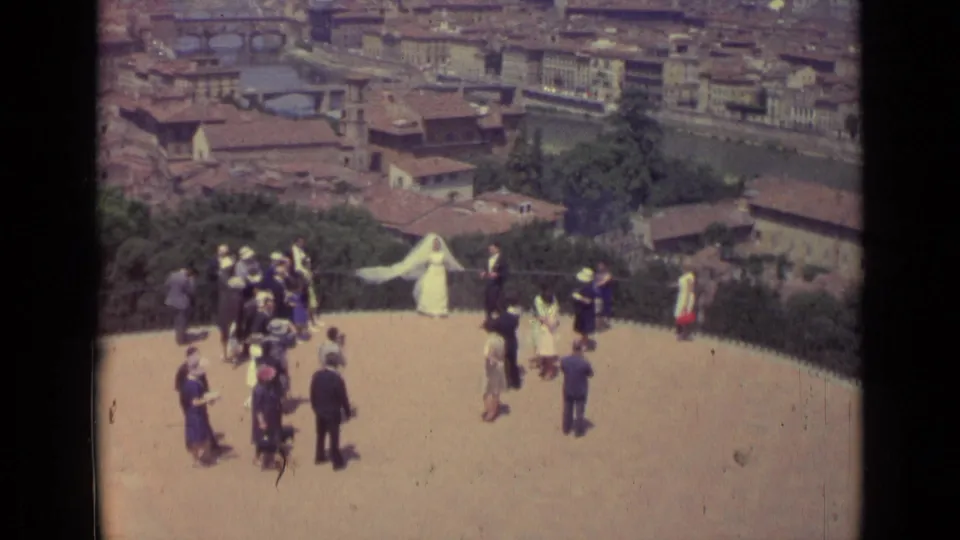 1962 Florence frame showing a wedding party on a hilltop overlook, with city rooftops, the Arno River, and bridges below.