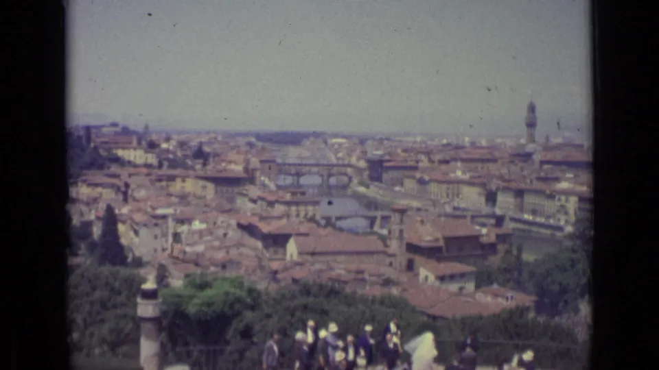 1962 8mm frame looking over Florence, with the Arno, bridges, tiled roofs, a stone balustrade, and visitors below.