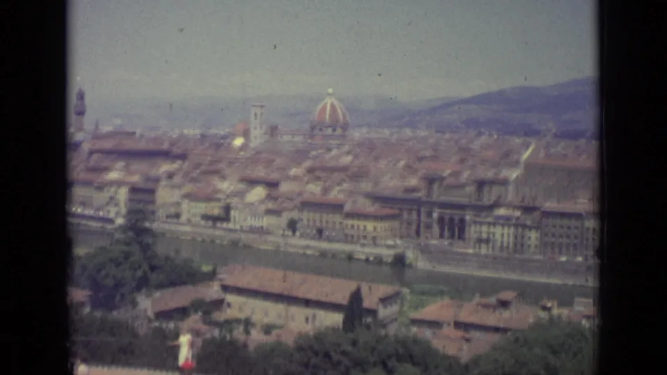 1962 8mm frame looking across Florence, Italy, with the Duomo, Arno River, hills, and a white-dressed wedding figure near the lower foreground.