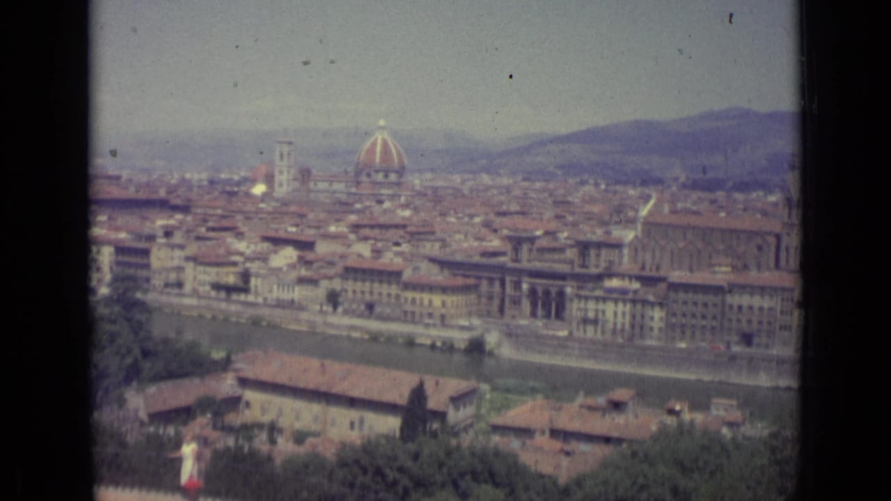 1962 8mm frame of Florence from above, showing the Duomo dome, dense terracotta roofs, the Arno riverfront, and hazy hills beyond.