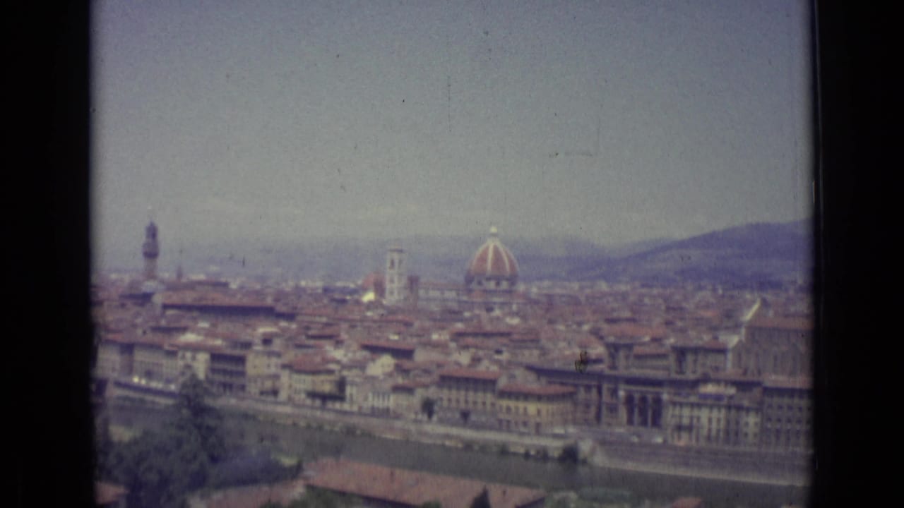 Florence cityscape with the Duomo dome, tower, riverfront blocks, rooftops, and hazy hills.