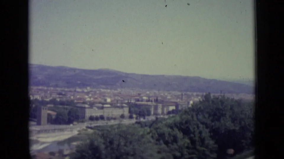 1962 8mm view over Florence, with dense buildings, a river, foreground trees, and distant hills seen from an overlook.
