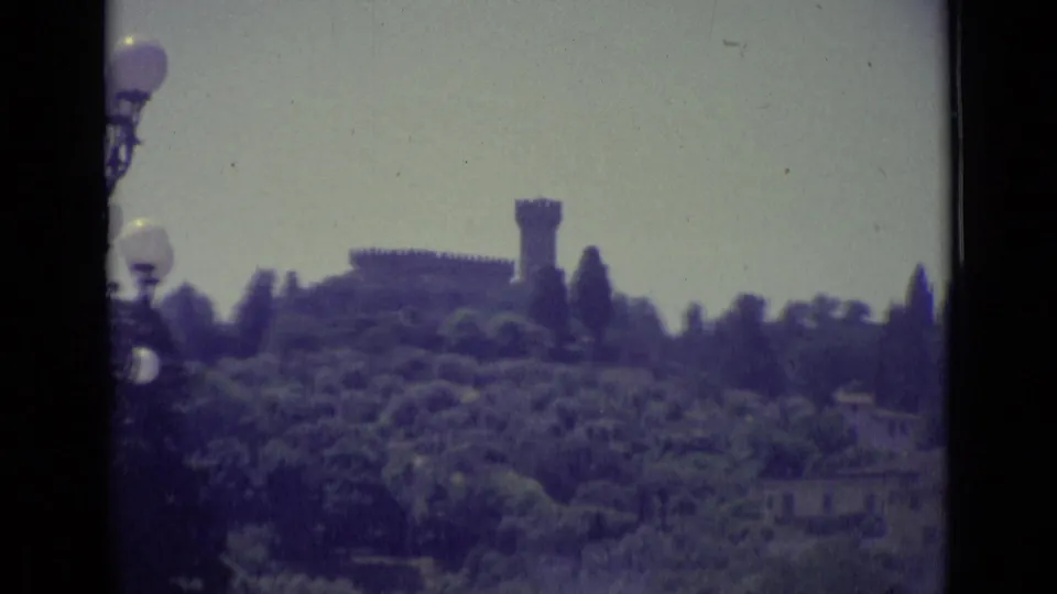 Soft 1962 8mm view of a Florence hillside with a tower or fortress rising above dense trees.