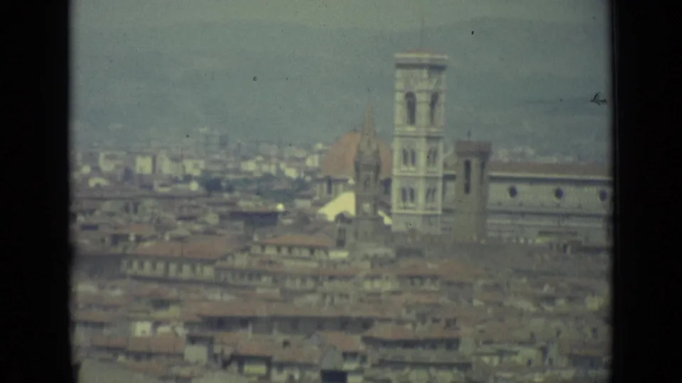 1962 8mm view over Florence rooftops toward the cathedral dome and bell tower, with the city spreading into a hazy background.