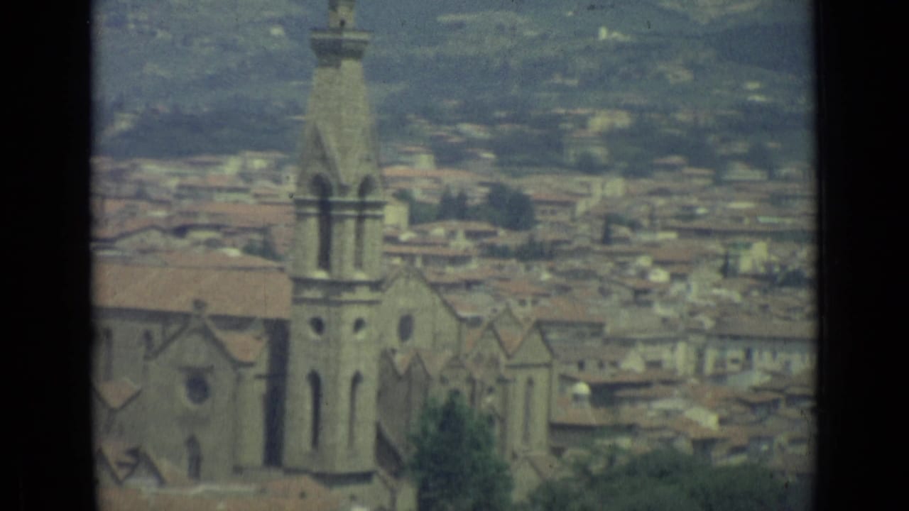 Church tower and roofline in Florence with the city and hills behind it.
