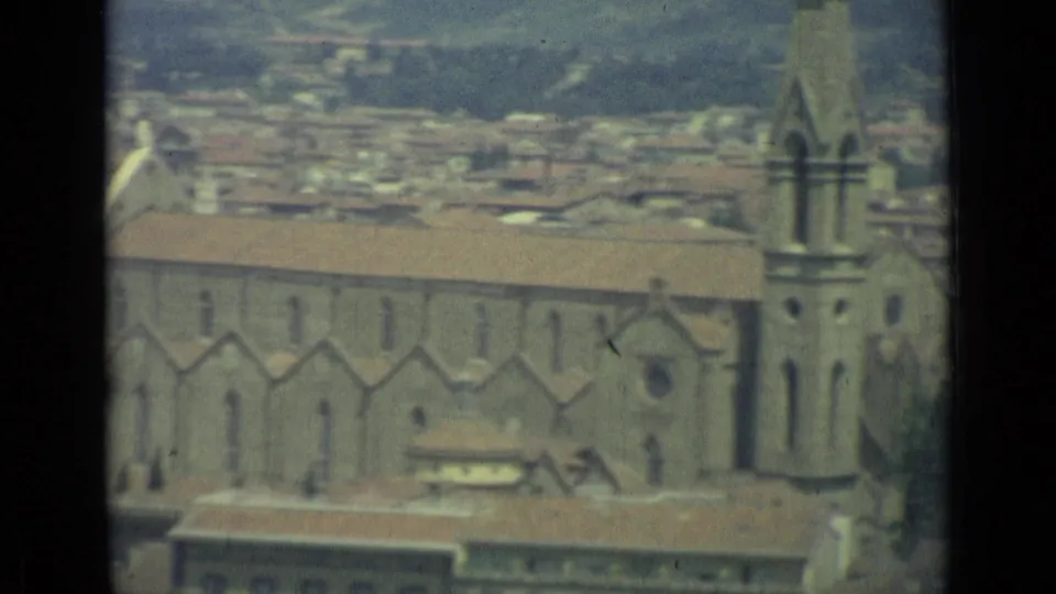 1962 Florence home-movie frame showing a large church facade and tower with the city stretching behind it.