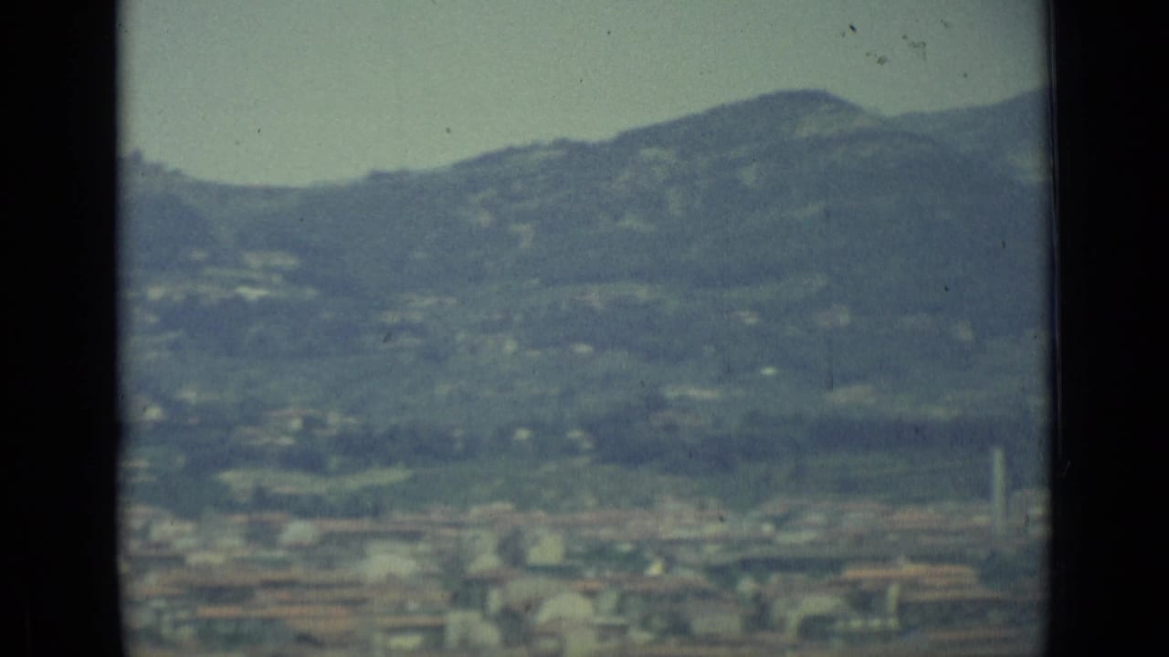 Hazy city below rolling hills seen through dark vertical frame edges.