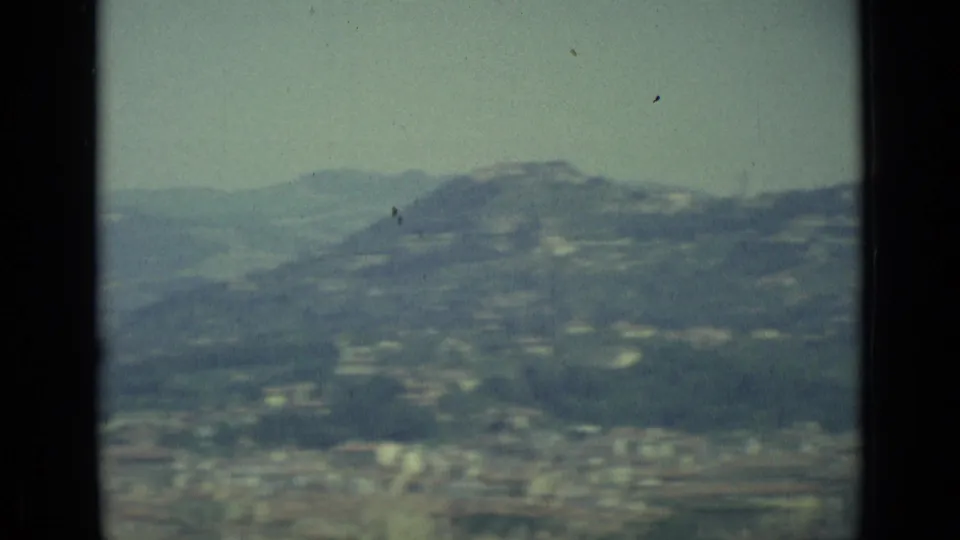 Soft 1962 Florence city-and-hill view with visible 8mm grain, dust, and muted color from an elevated position.