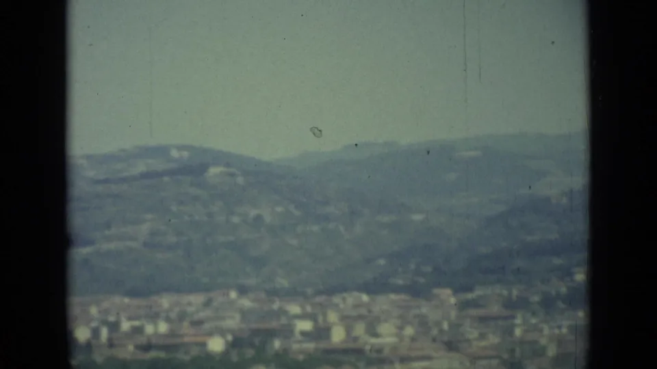 Final frame of a hazy Florence panorama, with distant urban blocks below low hills under a pale sky.