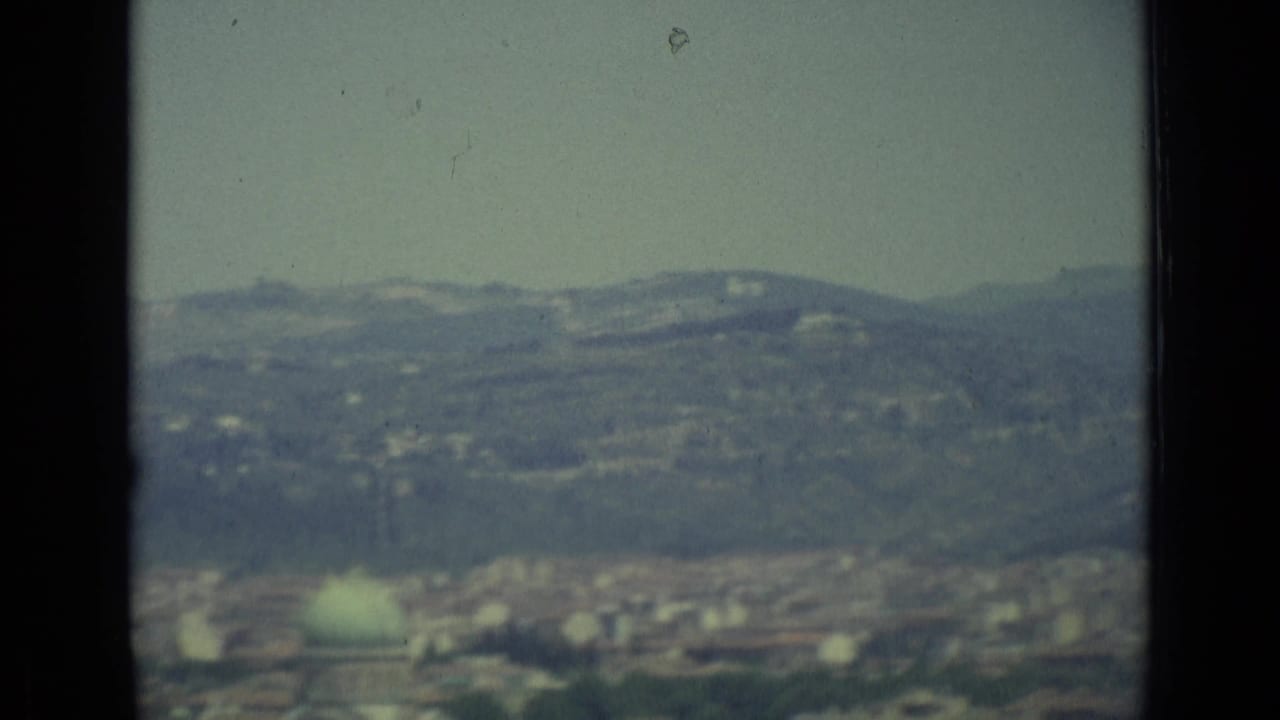 1962 8mm view of Florence from above, with soft distant hills, scattered rooftops, and a hazy pale sky.
