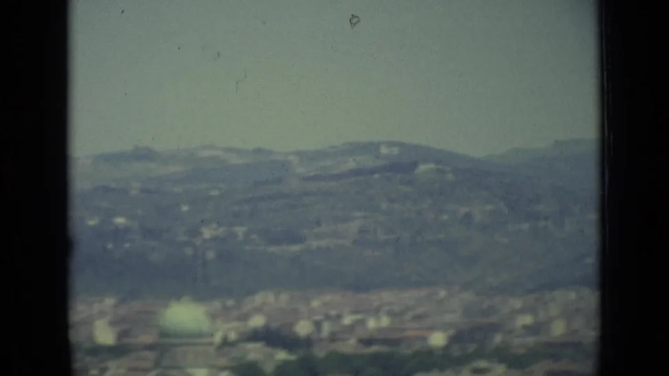 1962 8mm view of Florence from above, with soft distant hills, scattered rooftops, and a hazy pale sky.