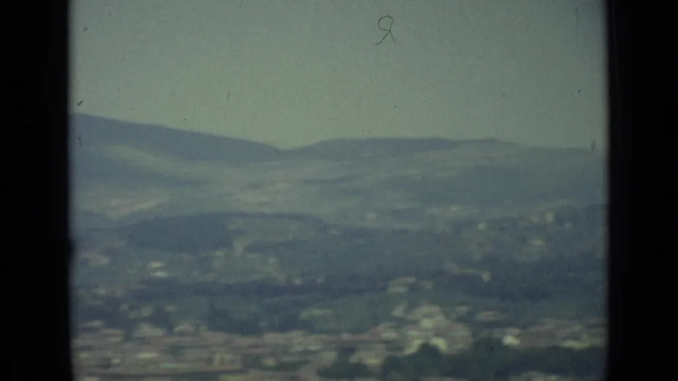 1962 8mm frame from an elevated Florence panorama, with layered hills above a soft, distant city edge.