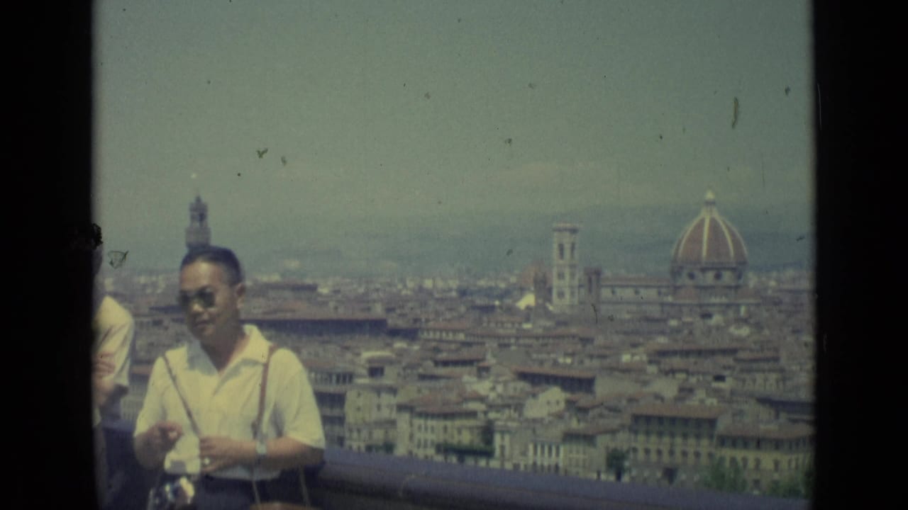 1962 Florence home-movie frame showing an adult man in sunglasses near an overlook, with rooftops, the Duomo, and Giotto's Campanile behind him.