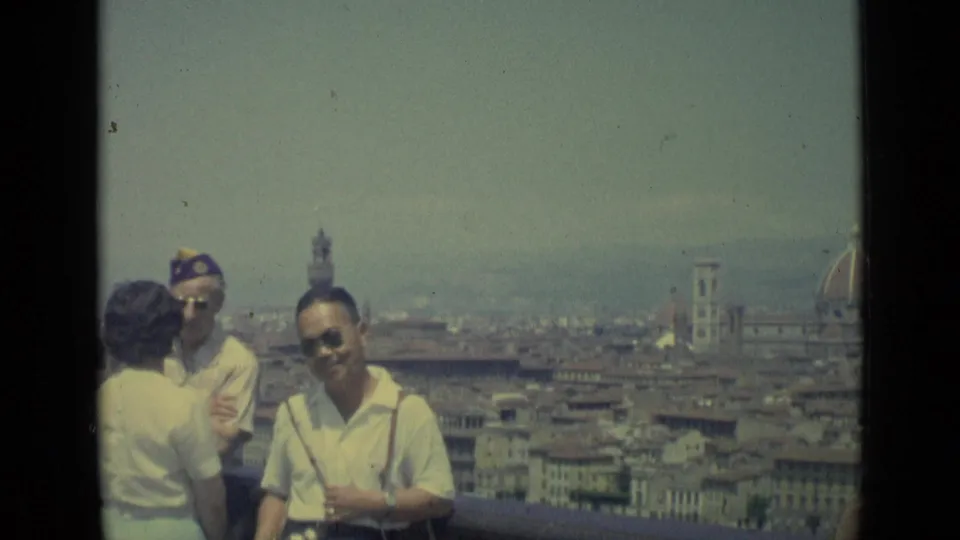 1962 Florence travel frame with adults chatting in the foreground and a man facing the camera, set against rooftops and landmark towers.