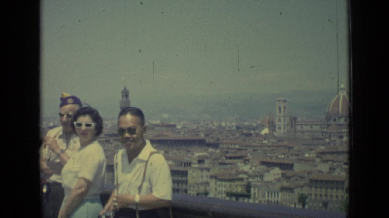 1962 Florence home-movie frame of tourists in sunglasses on a terrace overlooking rooftops, bell towers, and the Duomo dome.