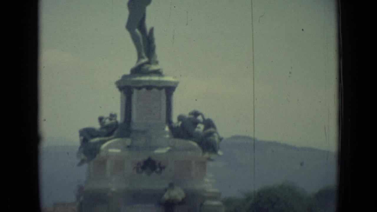 Close view of a large statue pedestal with sculptural figures and hills behind it.