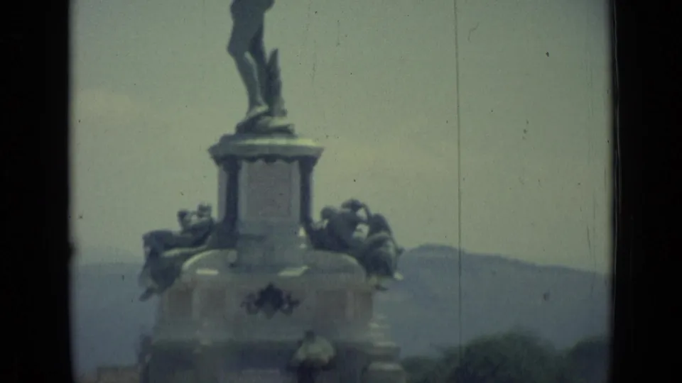 Soft 8mm frame from Florence, Italy, showing the lower part of a large public statue and pedestal against distant hills.
