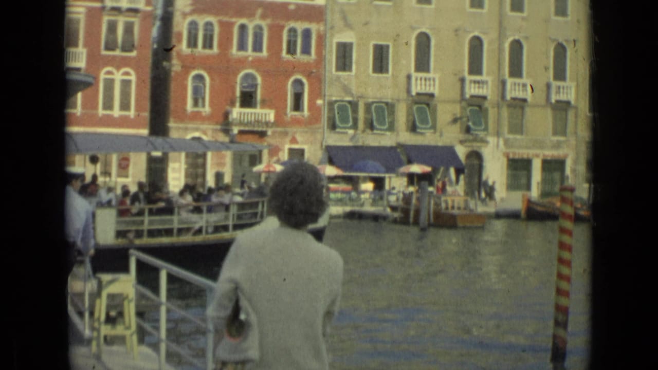Woman in a light jacket watches a boat approach along a canal dock.