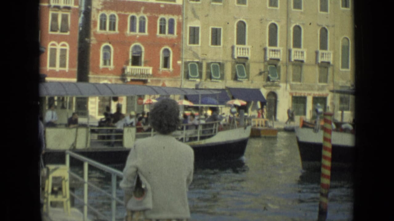 Woman watches canal traffic from a dock as a passenger boat passes.