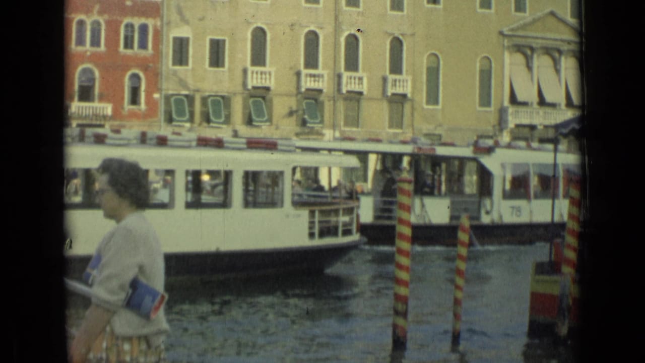 Pedestrian in foreground with a white canal boat and shuttered buildings behind.