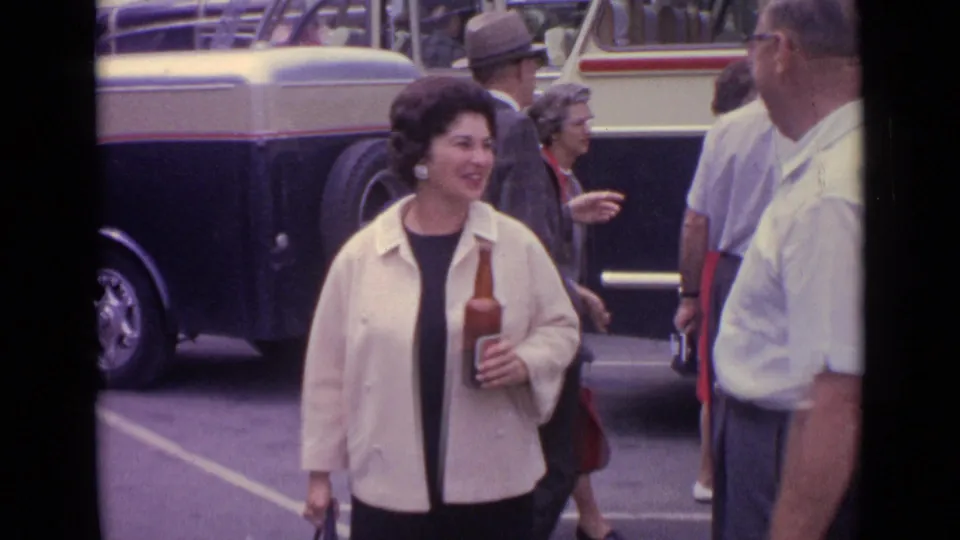 At the end of the short street moment, the woman holds the beer bottle and handbag while the man is partly cropped beside her near a bus.