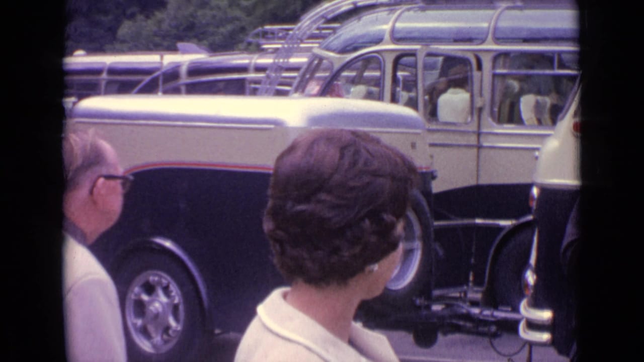 1962 Germany home-movie frame showing adults near a cream and black coach as travelers gather beside the vehicle.