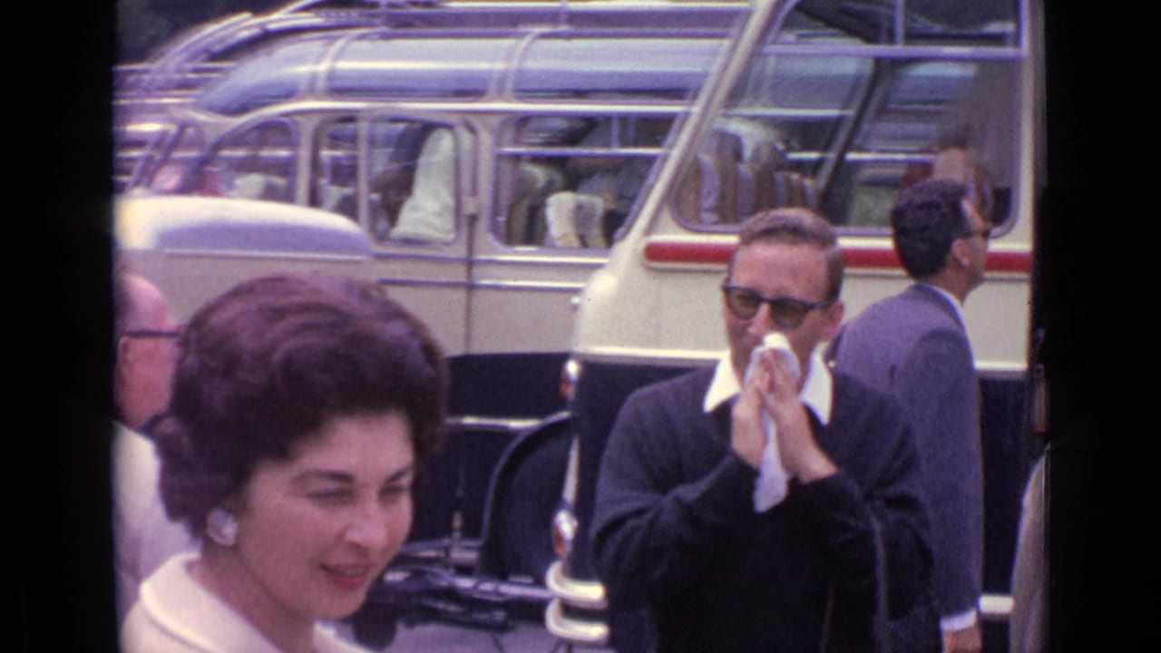 1962 Germany travel footage frame with a smiling woman near a bus and a man in sunglasses using a handkerchief.
