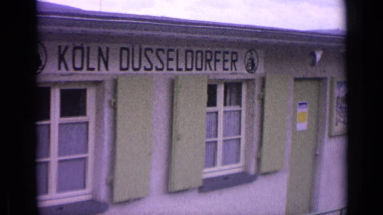 1962 Germany 8mm frame showing the Köln Düsseldorfer building sign, shuttered windows, and soft home-movie color cast.