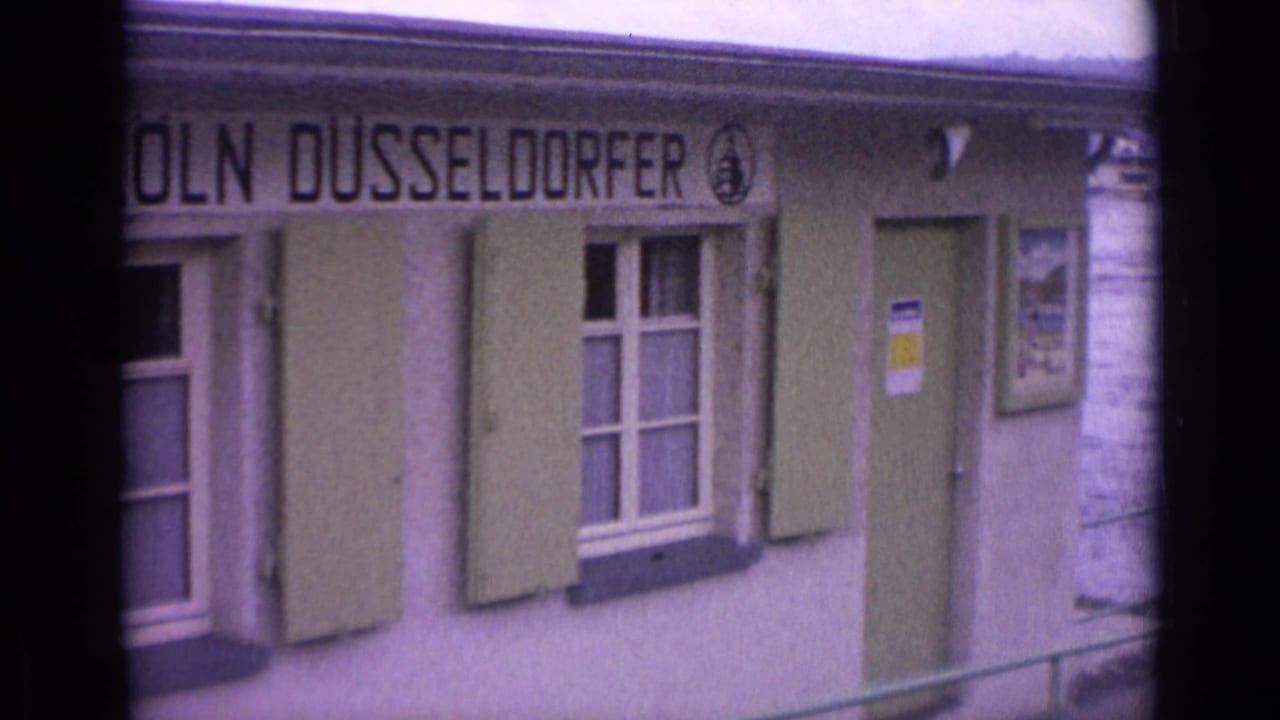 1962 Germany frame of the Köln Düsseldorfer riverside facade, with green shutters, a doorway, and railing near the edge of view.
